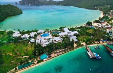Aerial view of Phi Phi Island Cabana Hotel, a gay-friendly hotel, with turquoise waters, lush greenery, and boats docked at the pier.
