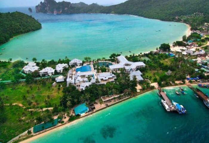Aerial view of Phi Phi Island Cabana Hotel, a gay-friendly hotel, with turquoise waters, lush greenery, and boats docked at the pier.