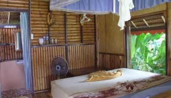 Phi Phi Relax Beach Resort's gay-friendly hotel room. Bamboo walls, bed with towel art, and a view of lush greenery. Tropical vibes.
