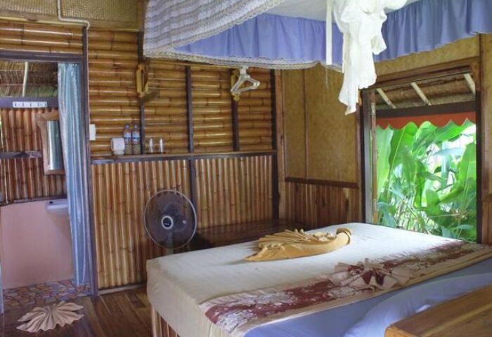 Phi Phi Relax Beach Resort's gay-friendly hotel room. Bamboo walls, bed with towel art, and a view of lush greenery. Tropical vibes.