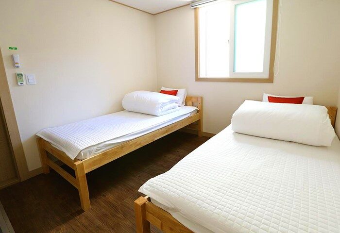 Philstay Itaewon Guesthouse room. Gay-friendly hotel with twin beds, white bedding, and wooden frames. Window provides natural light. Cozy stay.