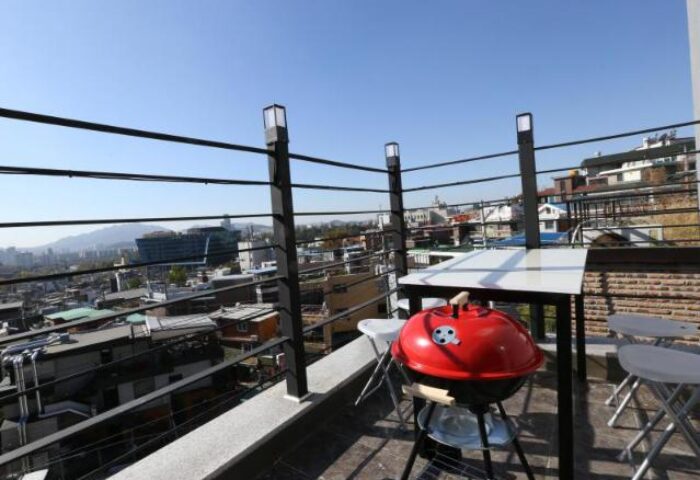 Rooftop view at Philstay Itaewon Guesthouse, a gay-friendly hotel. Features a grill, table, and chairs with a cityscape backdrop in Seoul, Korea.