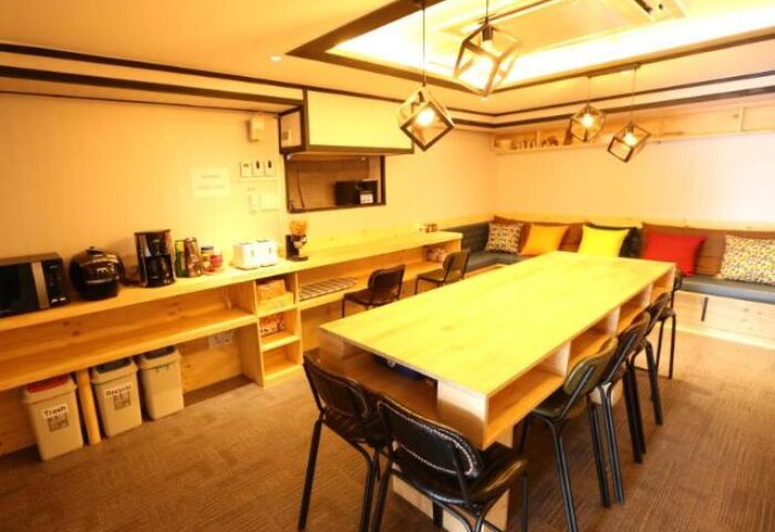 Philstay Itaewon Guesthouse's dining area. This gay-friendly hotel features a long table, chairs, and a kitchenette for a comfortable stay.