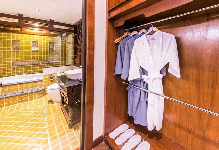 Phra Singh Village gay-friendly hotel room. Bathrobes and slippers in closet. Bathroom with tub, sink, and toilet visible. Thailand travel.