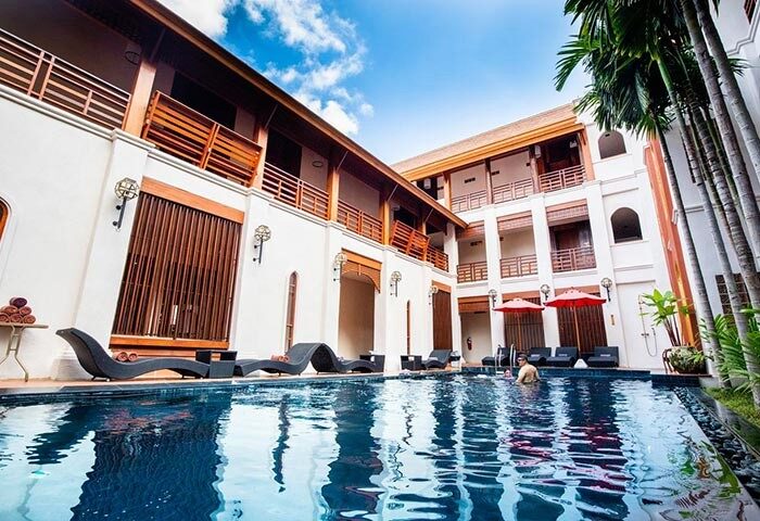 Phra Singh Village gay-friendly hotel pool. Man swimming. Balconies, sunbeds, and umbrellas surround the pool. Chiang Mai gay travel.