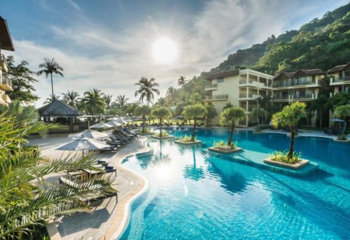 Phuket Marriott Resort & Spa, Merlin Beach pool. Gay-friendly hotel with palm trees, sun loungers, and clear blue water. Tropical paradise.