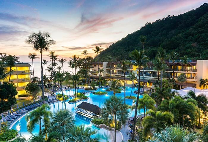 Phuket Marriott Resort & Spa, Merlin Beach aerial view. Gay-friendly hotel with pools, palm trees, and lush greenery at sunset.