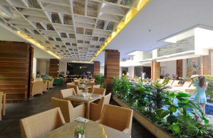 Ping Hotel Seminyak interior. Dining area with wicker chairs, pool view, and decorative ceiling. Gay-friendly hotel, stylish design.