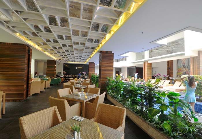 Ping Hotel Seminyak interior. Dining area with wicker chairs, pool view, and decorative ceiling. Gay-friendly hotel, stylish design.