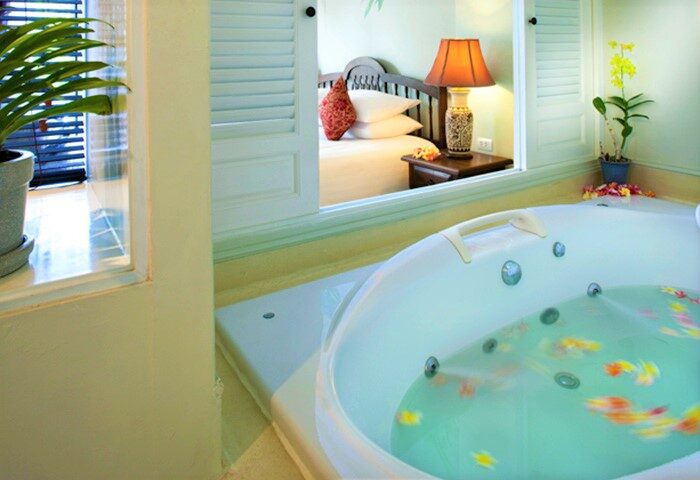 Ping Nakara Boutique Hotel and Spa gay-friendly room. Jacuzzi tub with flowers. Bedroom view through shuttered window. Luxury gay travel.