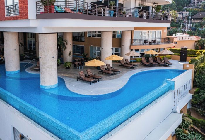 Pinnacle Resorts 180, gay-friendly hotel. Rooftop pool with lounge chairs and umbrellas. Modern building with balconies. Luxury gay travel.