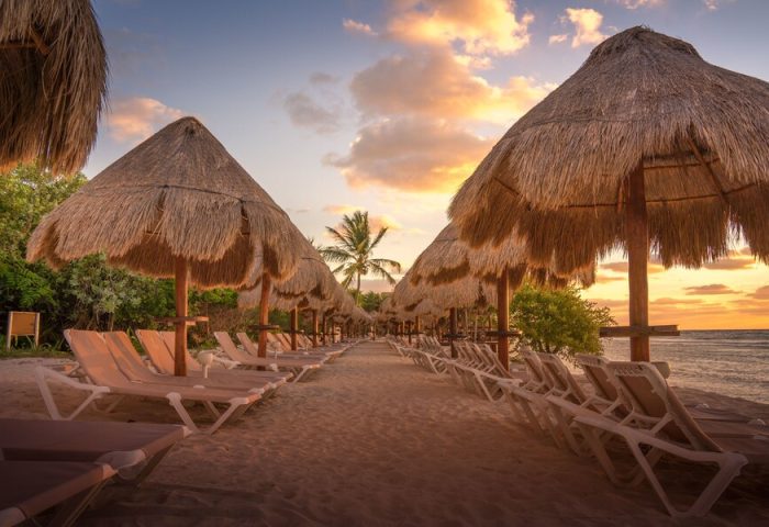 Beach at Platinum Yucatan Princess All Inclusive Suites Resort Adults Only. Thatched umbrellas and lounge chairs on the sand at sunset. Gay-friendly.