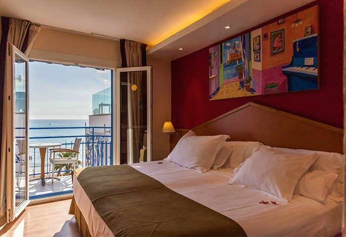 Gay-Friendly Hotel Platjador room with balcony overlooking the sea. Comfortable bed, colorful artwork. Ideal for gay travel & relaxation.