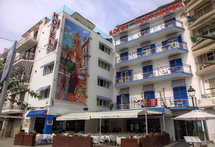 Gay-Friendly Hotel Platjador in Spain. White building with blue accents, balconies, restaurant, and mural. Gay travel destination.