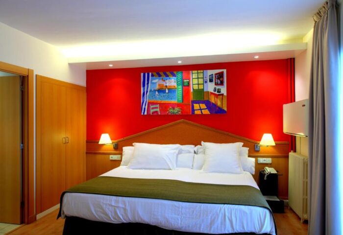 Gay-Friendly Hotel Platjador room. Red wall, painting above the bed. Comfortable, bright space. Ideal for gay travel. Platjador: your gay stay.