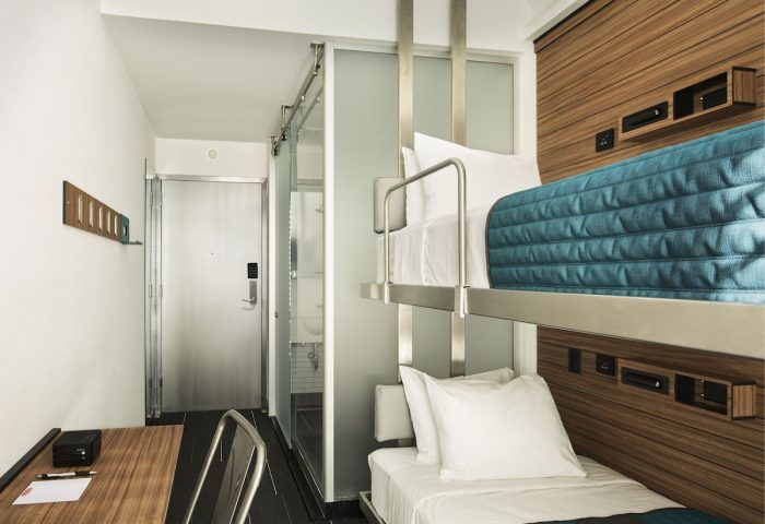 Pod Times Square gay-friendly hotel room. Bunk beds with blue accents, desk, and bathroom. Modern design for gay men travelers.