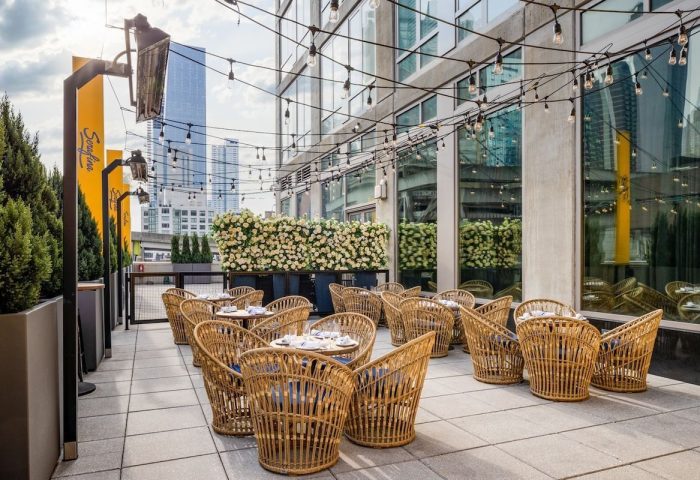Outdoor dining at gay-friendly Pod Times Square hotel. Wicker chairs surround tables under string lights. A modern, stylish NYC experience.