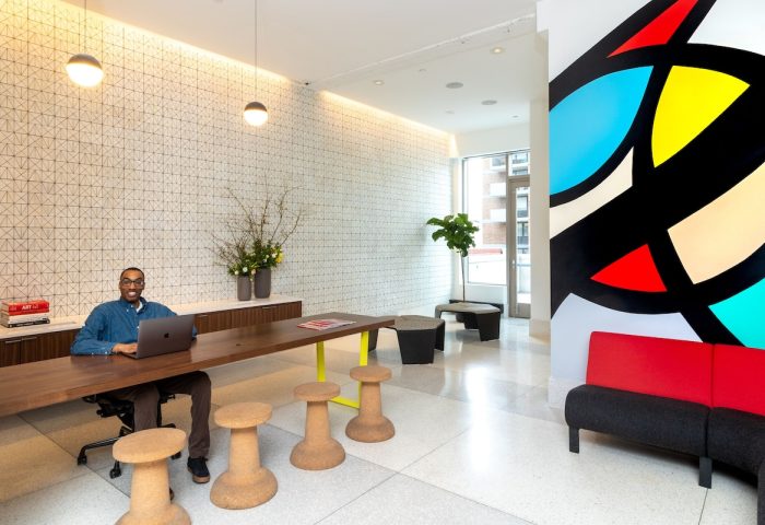 Pod Times Square gay-friendly hotel lobby view. Man working on laptop at communal table. Modern design, colorful art. Great for gay travel.