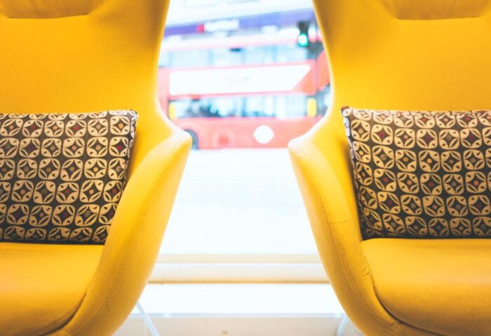 Point A Hotel London Westminster seating area. Yellow chairs with patterned pillows, red bus in background. Gay-friendly hotel.