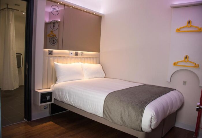 Point A Hotel London Westminster room. Gay-friendly hotel with a bed, shower, safe, and yellow hangers. Modern design for gay men travel.