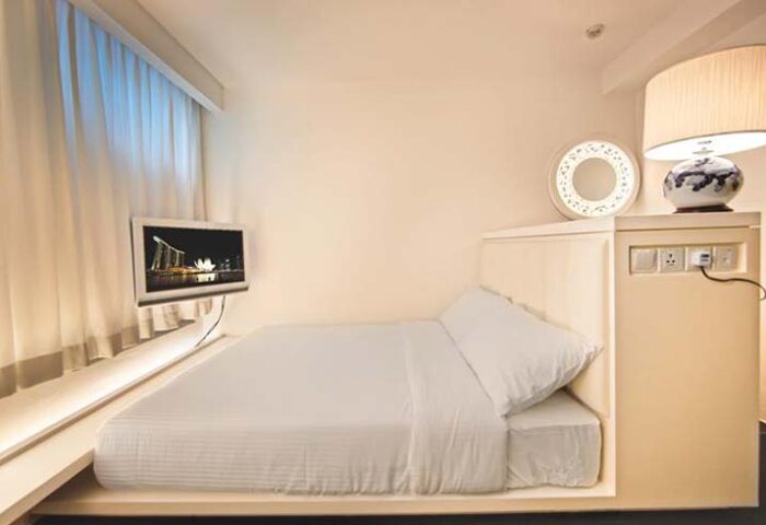 Porcelain Hotel by JL Asia room. Modern, compact design with TV, lamp, mirror, and outlets. Gay-friendly hotel option for travelers.