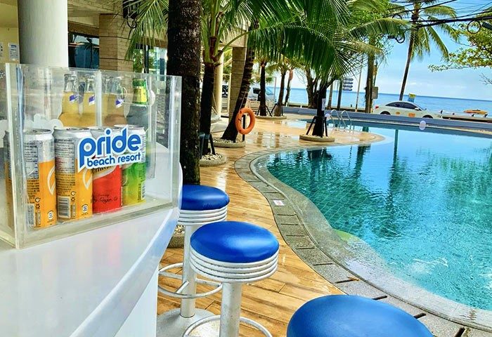 Pride Beach Resort adults-only gay-friendly hotel pool view. Bar stools, drinks, palm trees, and ocean create a tropical gay travel paradise.