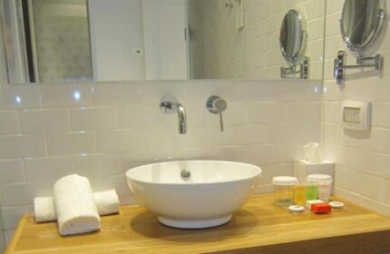 Bathroom at Prima City Hotel, Tel Aviv. Sink, towels, and toiletries on a wooden counter. Gay-friendly hotel for gay men travelers.