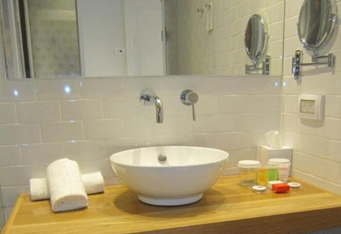 Bathroom at Prima City Hotel, Tel Aviv. Sink, towels, and toiletries on a wooden counter. Gay-friendly hotel for gay men travelers.