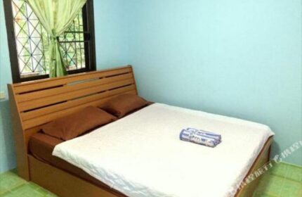Pudsa Bungalow gay-friendly hotel room. Interior view of bed with white sheets, brown pillows, and a window with green curtains.