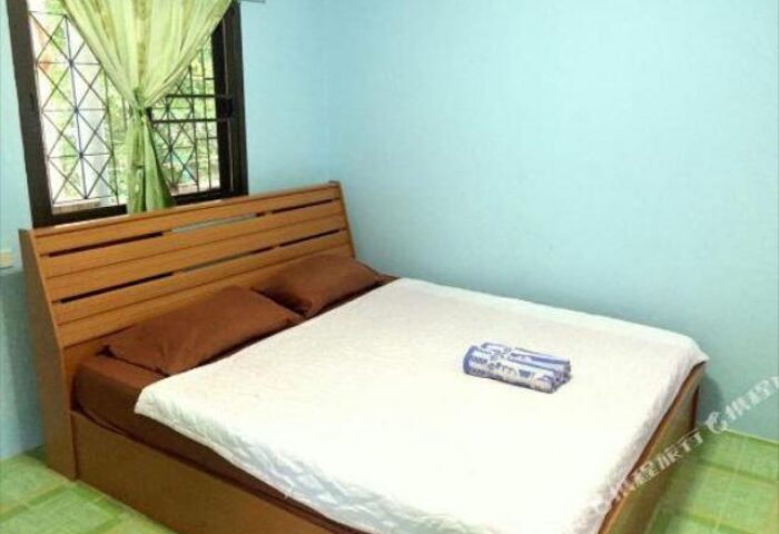Pudsa Bungalow gay-friendly hotel room. Interior view of bed with white sheets, brown pillows, and a window with green curtains.