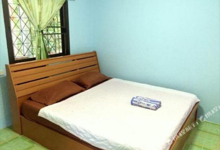 Pudsa Bungalow gay-friendly hotel room. Interior view of bed with white sheets, brown pillows, and a window with green curtains.