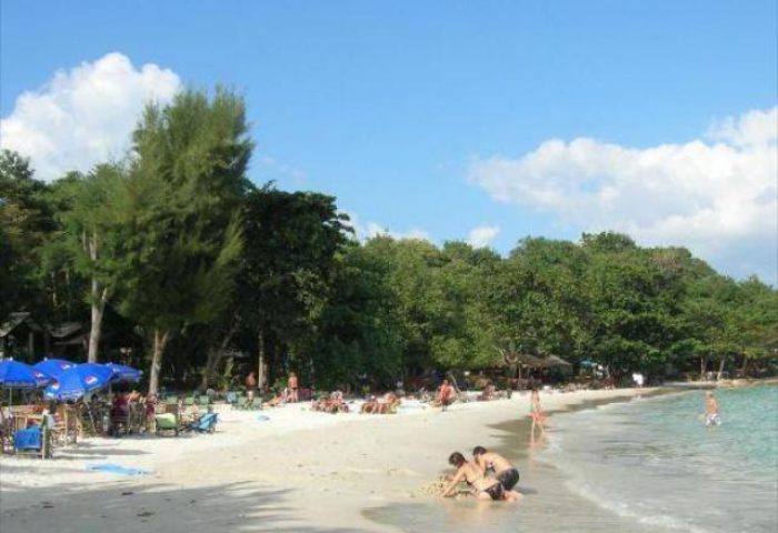 Beach view at gay-friendly Pudsa Bungalow. People relax on the sand, swim in the sea. A tropical paradise for gay men's travel.