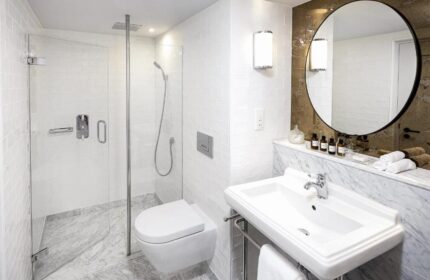 Bathroom at the Gay-Friendly Pulitzer Amsterdam Hotel. Features a shower, toilet, sink, and round mirror. Ideal for gay men travelers.