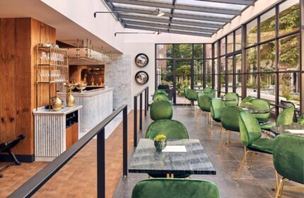 Pulitzer Amsterdam gay-friendly hotel: Interior view of the restaurant with green velvet chairs, marble tables, and a glass ceiling.