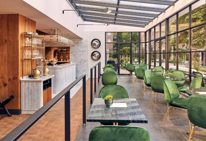 Pulitzer Amsterdam gay-friendly hotel: Interior view of the restaurant with green velvet chairs, marble tables, and a glass ceiling.