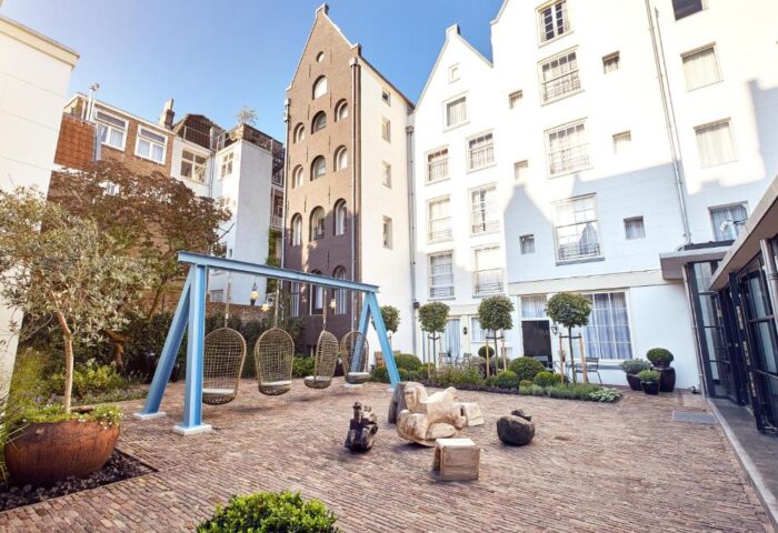 Pulitzer Amsterdam gay-friendly hotel courtyard. Egg-shaped swings hang over brick ground. Unique building architecture in Amsterdam.