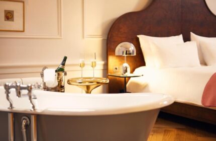 Pulitzer Amsterdam gay-friendly hotel room. Bathtub, champagne bucket, and flutes on a gold table. Bed with white linens in background.