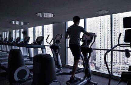 Pullman Jakarta Central Park Hotel's gym. Man on elliptical trainer with city view. Gay-friendly hotel fitness center.