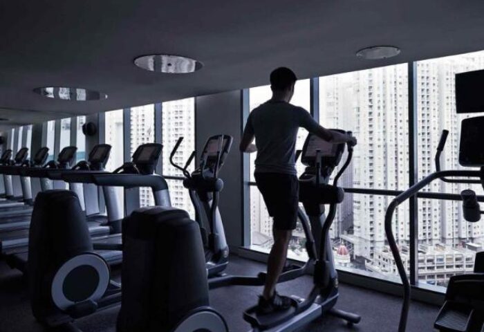 Pullman Jakarta Central Park Hotel's gym. Man on elliptical trainer with city view. Gay-friendly hotel fitness center.