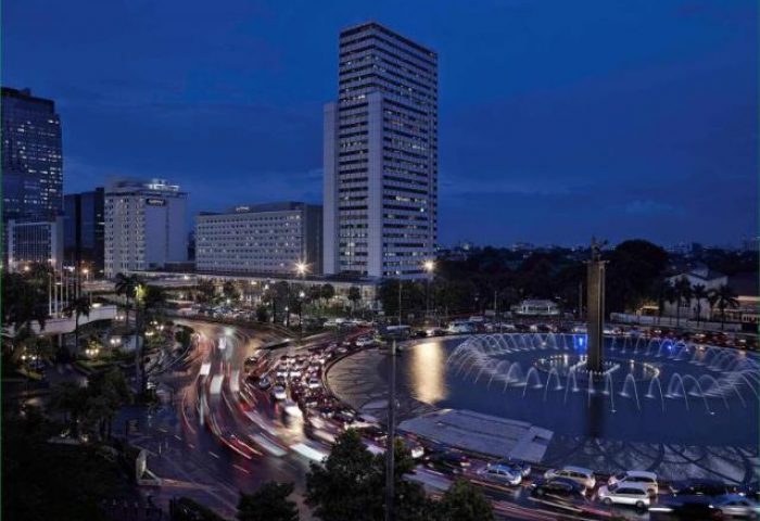 Night view of Pullman Jakarta Indonesia, a gay-friendly hotel, with the Welcome Monument fountain and city skyline. Jakarta travel.