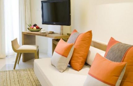 Pullman Pattaya Hotel G interior. Gay-friendly hotel room featuring a sofa, TV, desk with fruit, and chair. Modern design, comfortable space.