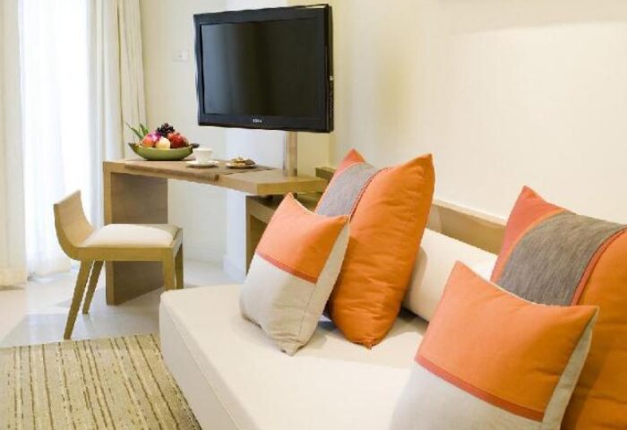 Pullman Pattaya Hotel G interior. Gay-friendly hotel room featuring a sofa, TV, desk with fruit, and chair. Modern design, comfortable space.
