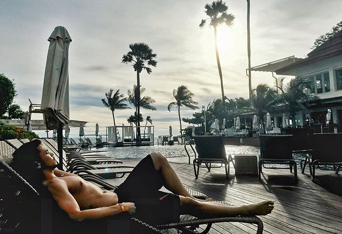 Gay man relaxing poolside at Pullman Pattaya Hotel G. Palm trees, ocean view, and lounge chairs create a serene gay-friendly travel destination.