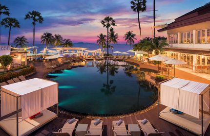 Pullman Pattaya Hotel G pool view at dusk. Gay-friendly hotel with palm trees, lounge chairs, and ocean view. A serene travel destination.