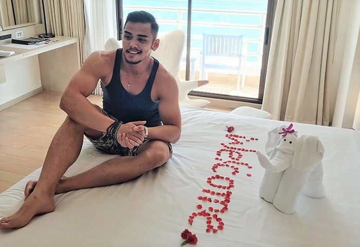 Gay-friendly Pullman Pattaya Hotel G: Man on bed with rose petals spelling Welcome and towel elephant. Luxury gay travel in Thailand.