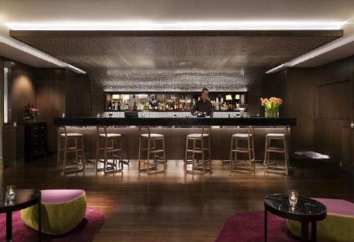 Bar area at the gay-friendly Pullman Sydney Hyde Park hotel. Stylish interior, stools at the bar, and a bartender serving drinks.