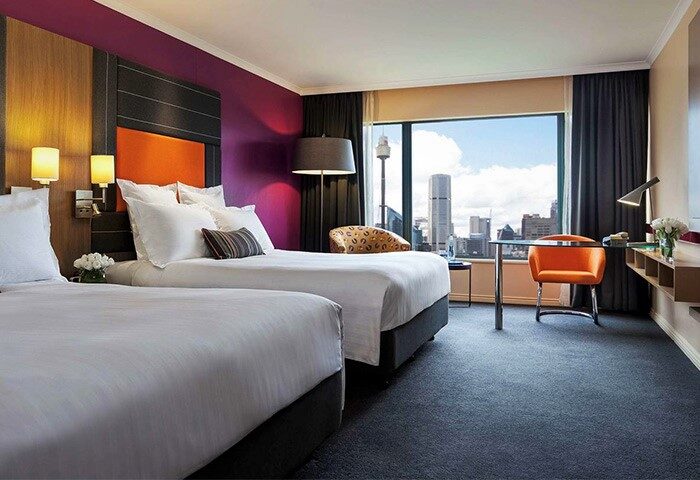 Gay-friendly Pullman Sydney Hyde Park hotel room with two beds, city view, desk, and chair. Ideal for gay travel in Sydney, Australia.