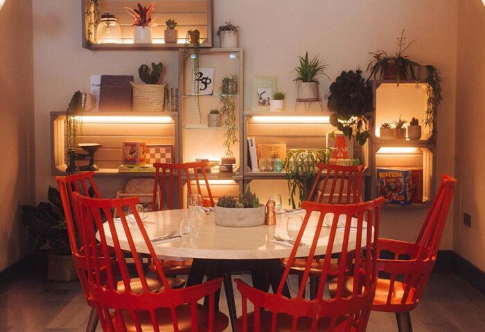 Qbic London City, a gay-friendly, pet-friendly hotel. Round table with red chairs, plants on shelves. Modern design.