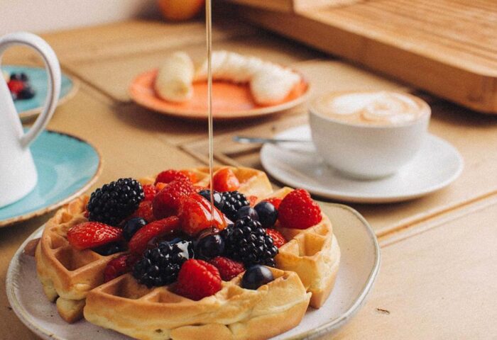 Breakfast at Gay-Friendly Hotel Qbic London City: Waffles topped with fresh berries and syrup, alongside a latte and banana slices.