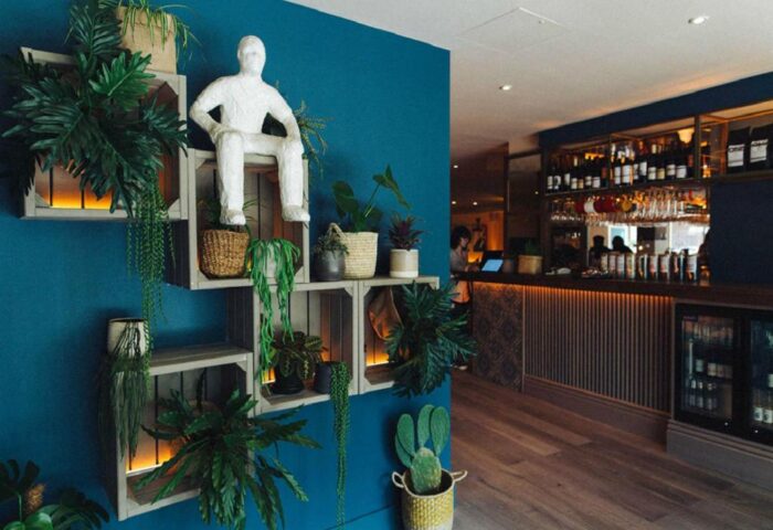 Qbic London City gay-friendly hotel's stylish decor. A figure sits atop wooden crates filled with plants near the bar. Pet-friendly.